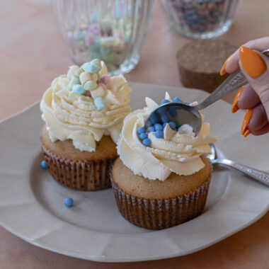 Finished muffins topped with whipped cream and pastel sprinkles on a plate, a spoon diving in.