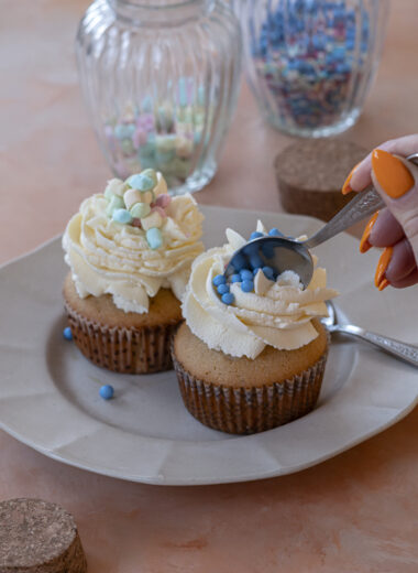 Finished muffins topped with whipped cream and pastel sprinkles on a plate, a spoon diving in.
