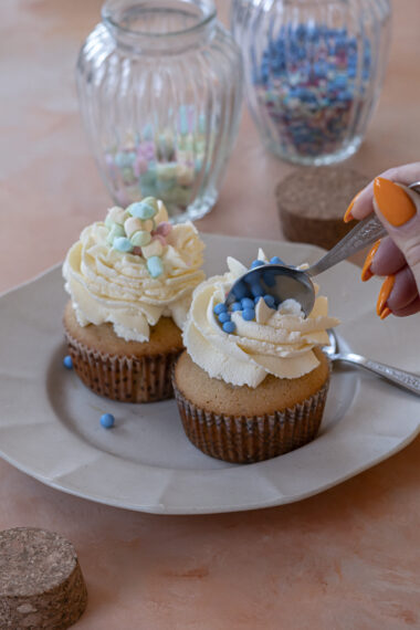 Finished muffins topped with whipped cream and pastel sprinkles on a plate, a spoon diving in.