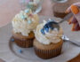 Finished muffins topped with whipped cream and pastel sprinkles on a plate, a spoon diving in.