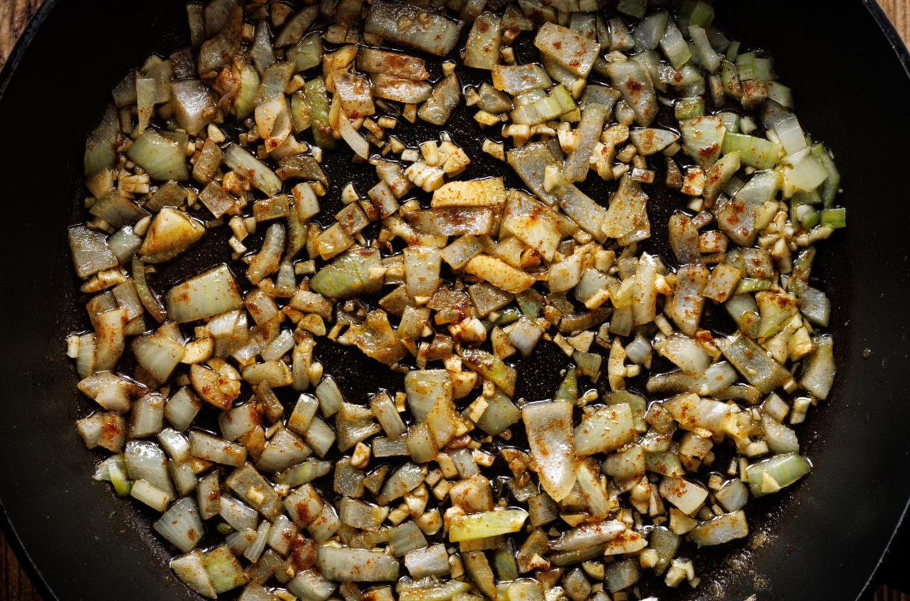 Chopped onion and garlic with paprika sautéing in a black skillet, the first step of healthy sloppy joes