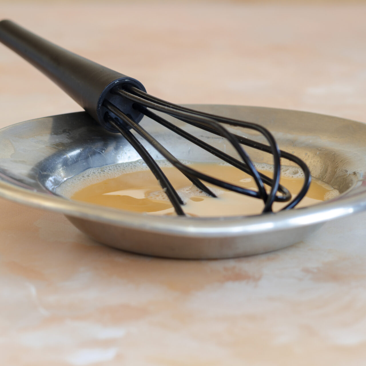 Whisk resting in a bowl with egg and milk mixture, starting muffin batter preparation.