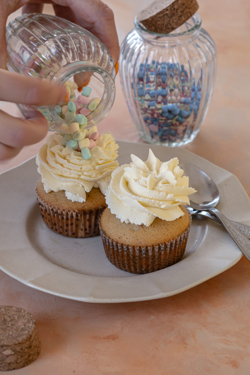 Adding little colorful marshmallows on whipped cream topped muffins for a playful finish.