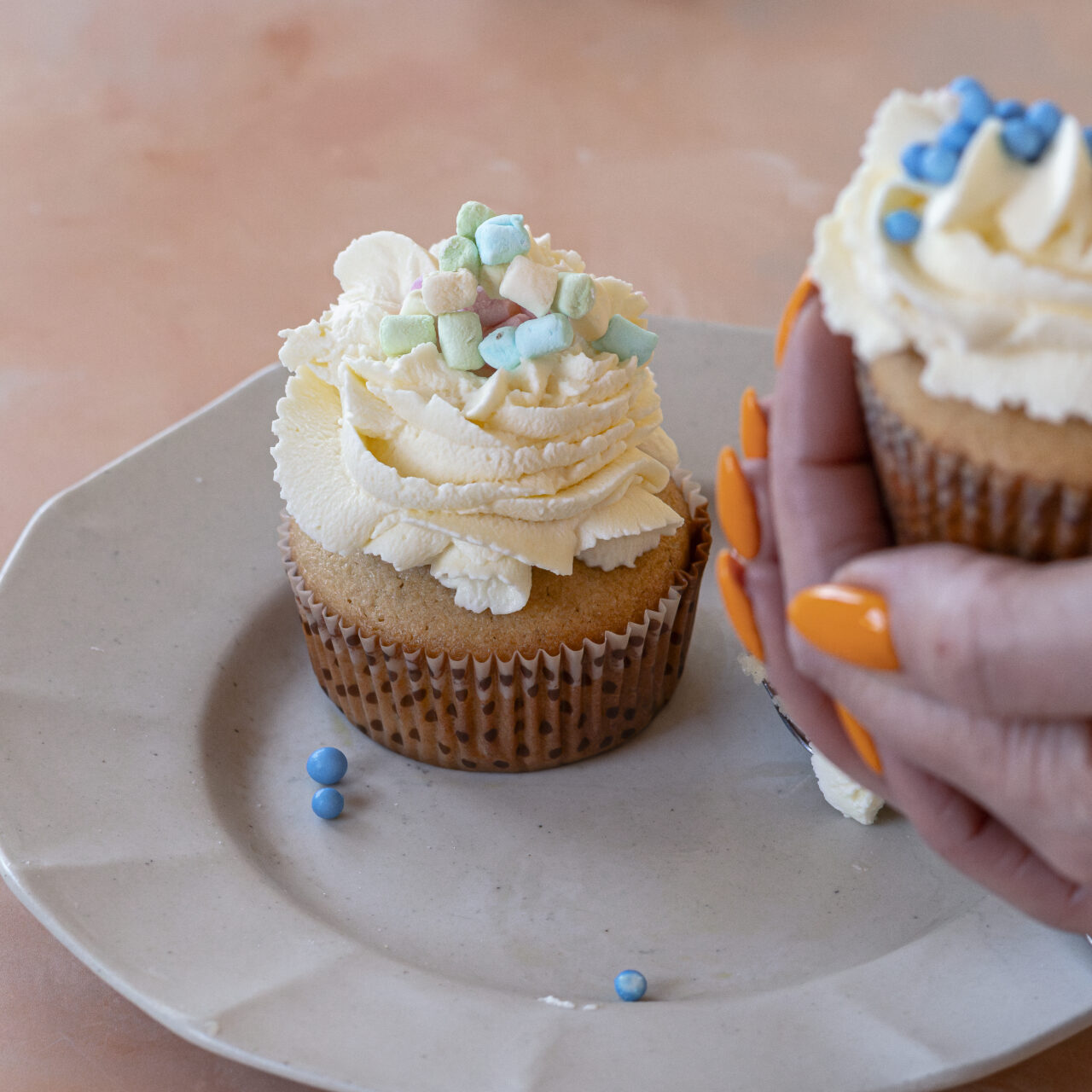 Close-up of a decorated muffin with whipped cream and pastel toppings, ready to enjoy in a woman's hand.