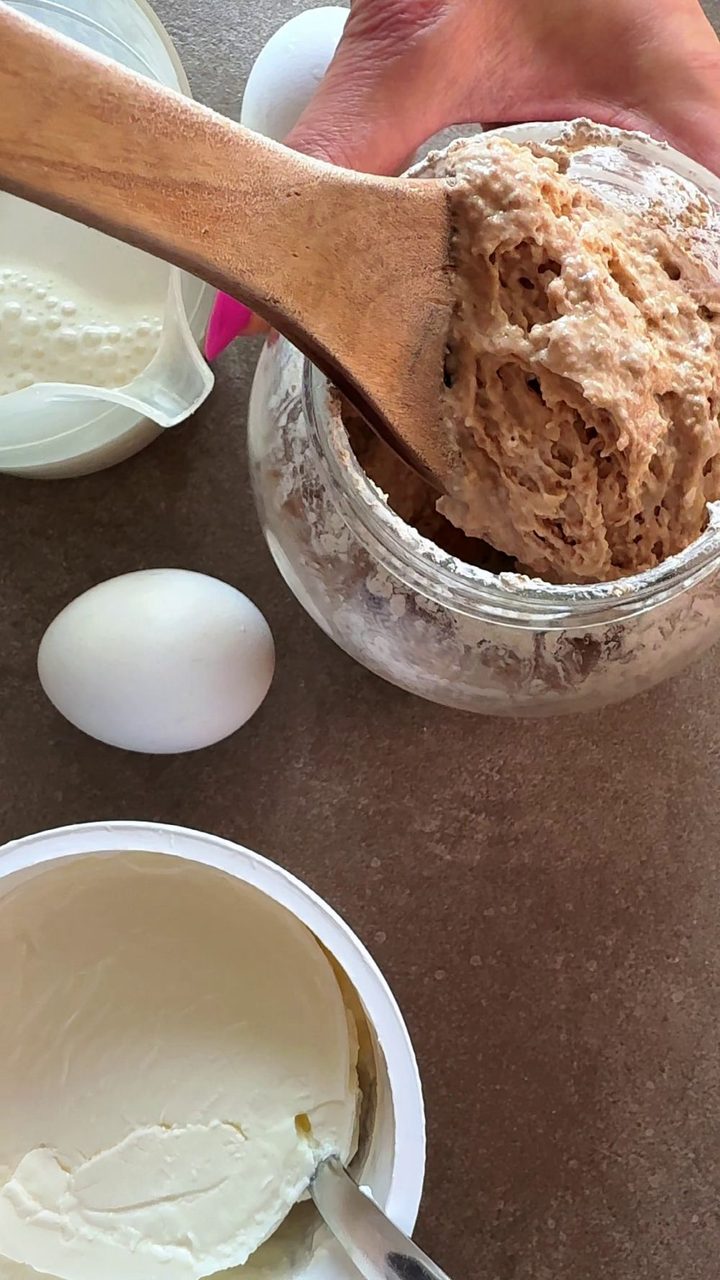 Sourdough starter on a wooden spoon above the jar, with an egg, Greek yogurt and cream