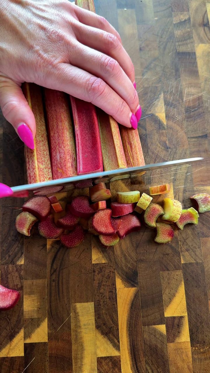 Chopping fresh rhubarb stalks into small pieces on a wooden cutting board