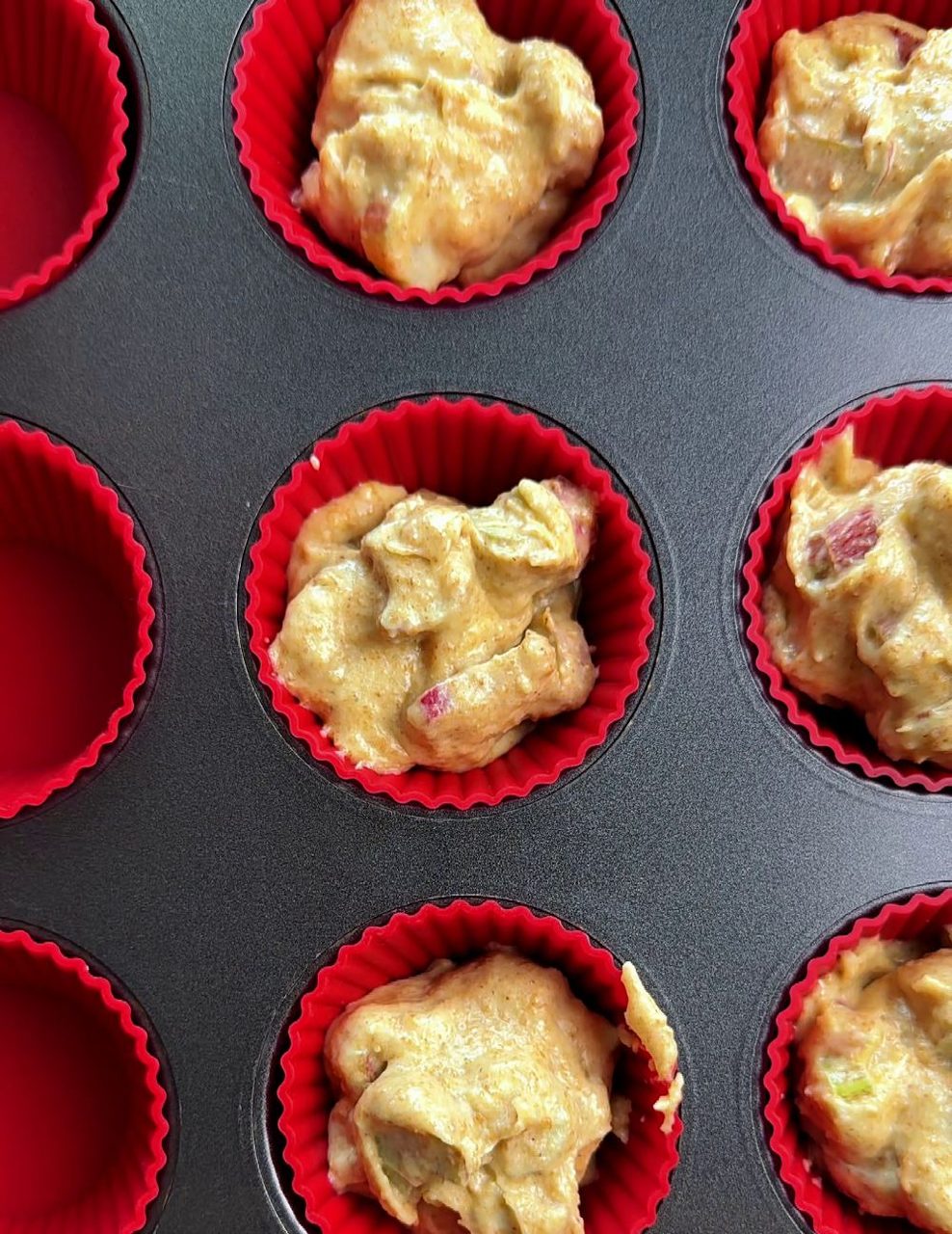 Rhubarb muffin batter filled into red silicone cups in a muffin tin, ready to bake